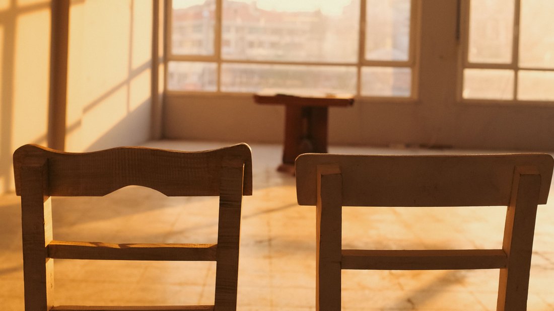 Two empty wooden chairs facing a sunlit window