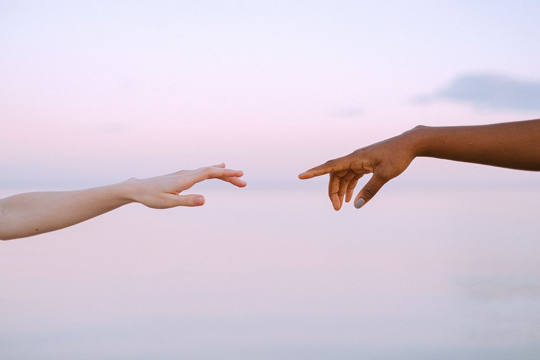 Two hands reaching toward each other against a dusk sky