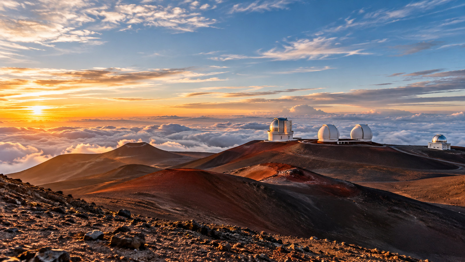 Observatory domes on the red slopes of Mauna Kea above a sea of clouds at sunrise